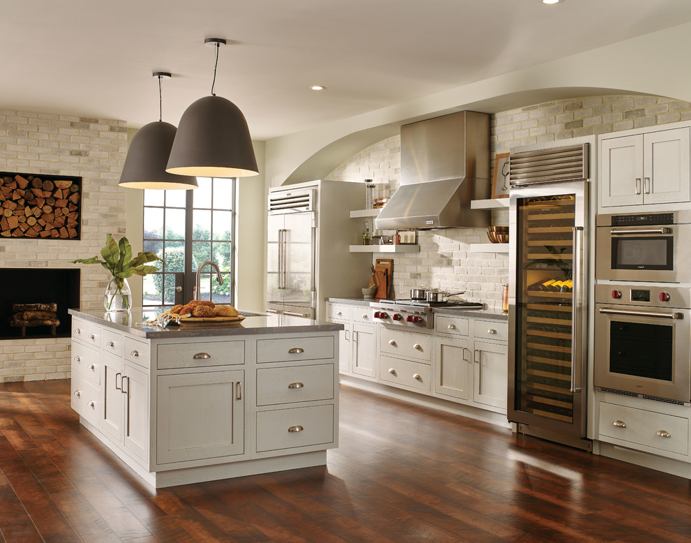Aménagement d'une cuisine américaine classique avec des portes de placard blanches, un électroménager en acier inoxydable, îlot, un sol marron et un plan de travail gris.