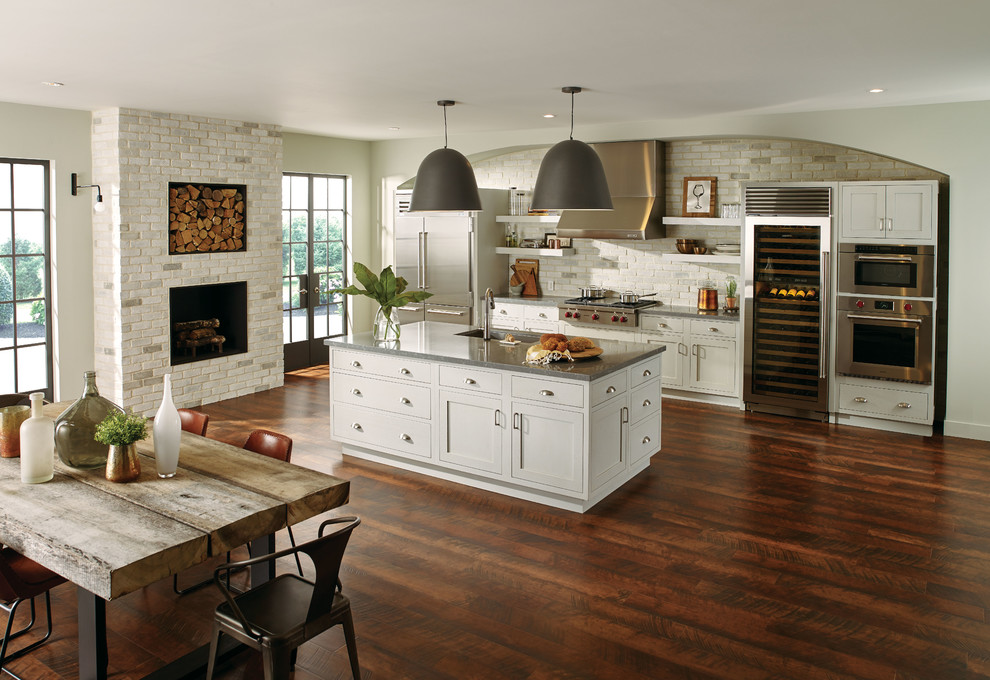 Large elegant single-wall dark wood floor and brown floor eat-in kitchen photo in New York with an undermount sink, shaker cabinets, white cabinets, limestone countertops, beige backsplash, brick backsplash, stainless steel appliances and an island