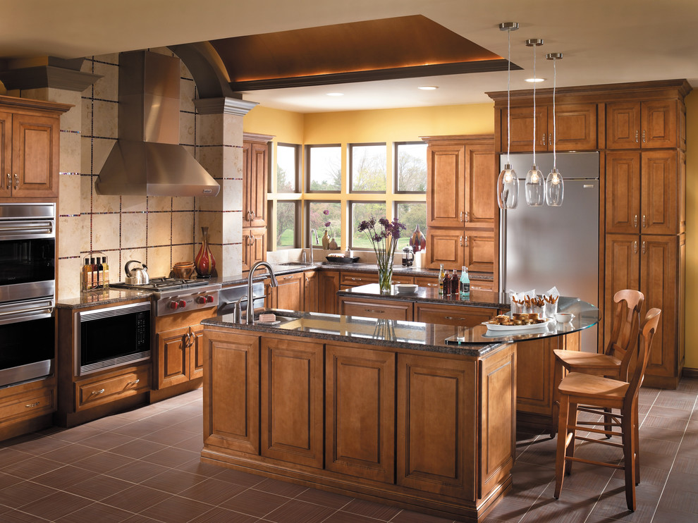 Example of a large transitional l-shaped ceramic tile and brown floor open concept kitchen design in Other with raised-panel cabinets, medium tone wood cabinets, glass countertops, stainless steel appliances, an island, an undermount sink, beige backsplash and stone tile backsplash