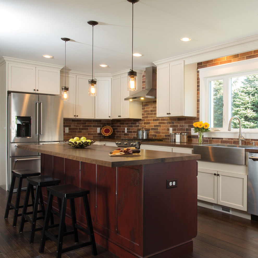 Eat-in kitchen - large traditional l-shaped dark wood floor and brown floor eat-in kitchen idea in Other with a farmhouse sink, recessed-panel cabinets, red cabinets, brown backsplash, brick backsplash, stainless steel appliances and an island
