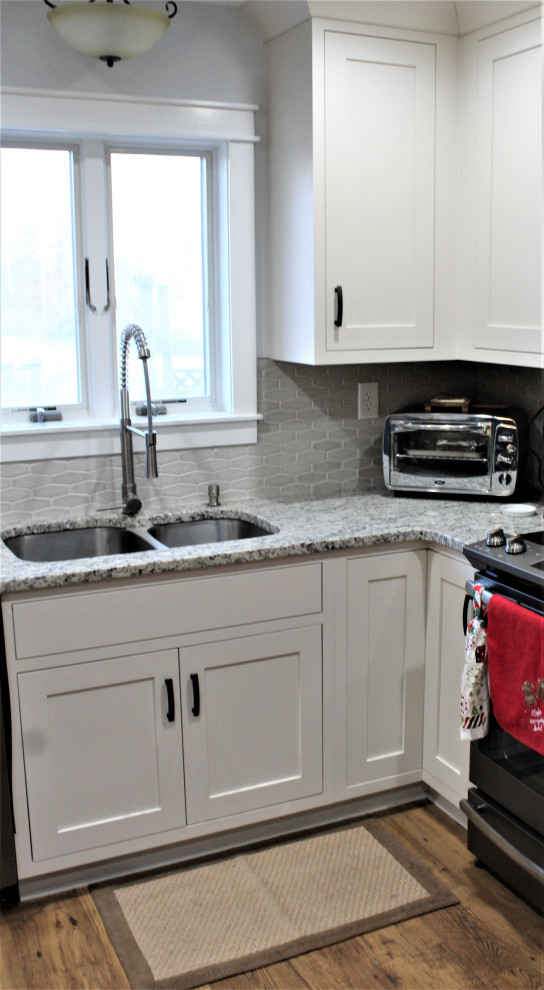Example of a large trendy l-shaped medium tone wood floor and brown floor eat-in kitchen design in Detroit with shaker cabinets, granite countertops, stainless steel appliances, an island, an undermount sink, white cabinets, gray backsplash, stone tile backsplash and gray countertops