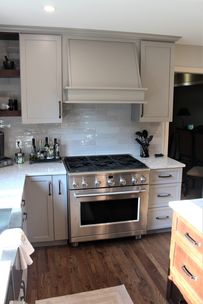 Design ideas for a large classic galley kitchen/diner in Detroit with a belfast sink, shaker cabinets, grey cabinets, engineered stone countertops, grey splashback, ceramic splashback, stainless steel appliances, medium hardwood flooring, an island, brown floors and grey worktops.