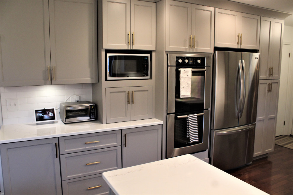 Exempel på ett litet klassiskt grå grått kök, med luckor med infälld panel, grå skåp, vitt stänkskydd, rostfria vitvaror, en undermonterad diskho, bänkskiva i kvarts, stänkskydd i keramik, mellanmörkt trägolv, en halv köksö och brunt golv