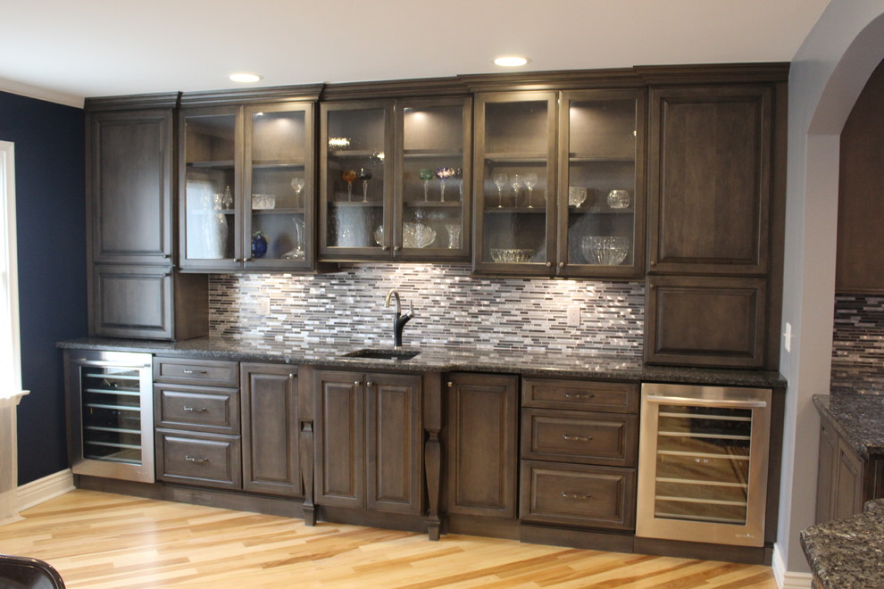 This is an example of a large classic kitchen/diner in Detroit with a submerged sink, raised-panel cabinets, medium wood cabinets, granite worktops, grey splashback, mosaic tiled splashback, stainless steel appliances, light hardwood flooring and a breakfast bar.