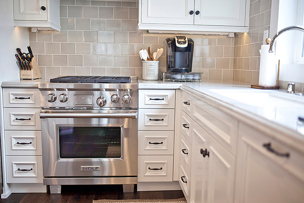 Klassisk inredning av ett litet kök, med en undermonterad diskho, skåp i shakerstil, vita skåp, bänkskiva i kvartsit, beige stänkskydd, stänkskydd i keramik, rostfria vitvaror, mörkt trägolv och en köksö