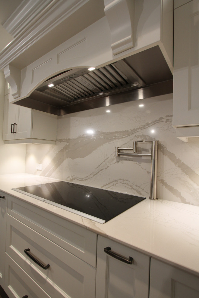 Design ideas for a large contemporary l-shaped kitchen/diner in Toronto with a submerged sink, recessed-panel cabinets, white cabinets, engineered stone countertops, grey splashback, stone slab splashback, stainless steel appliances, medium hardwood flooring, an island, brown floors and grey worktops.
