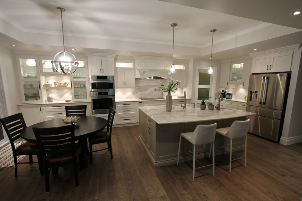 Inredning av ett modernt stort grå grått kök, med en undermonterad diskho, luckor med infälld panel, vita skåp, bänkskiva i kvarts, grått stänkskydd, stänkskydd i sten, rostfria vitvaror, mellanmörkt trägolv, en köksö och brunt golv