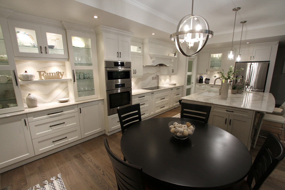 This is an example of a large contemporary l-shaped kitchen/diner in Toronto with a submerged sink, recessed-panel cabinets, white cabinets, engineered stone countertops, grey splashback, stone slab splashback, stainless steel appliances, medium hardwood flooring, an island, brown floors and grey worktops.