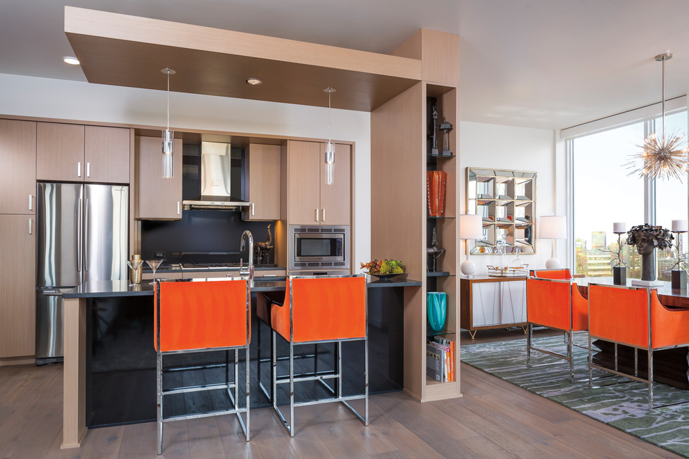 Photo of a medium sized contemporary galley kitchen/diner in Chicago with flat-panel cabinets, light wood cabinets, black splashback, stainless steel appliances, an island, brown floors, composite countertops and medium hardwood flooring.