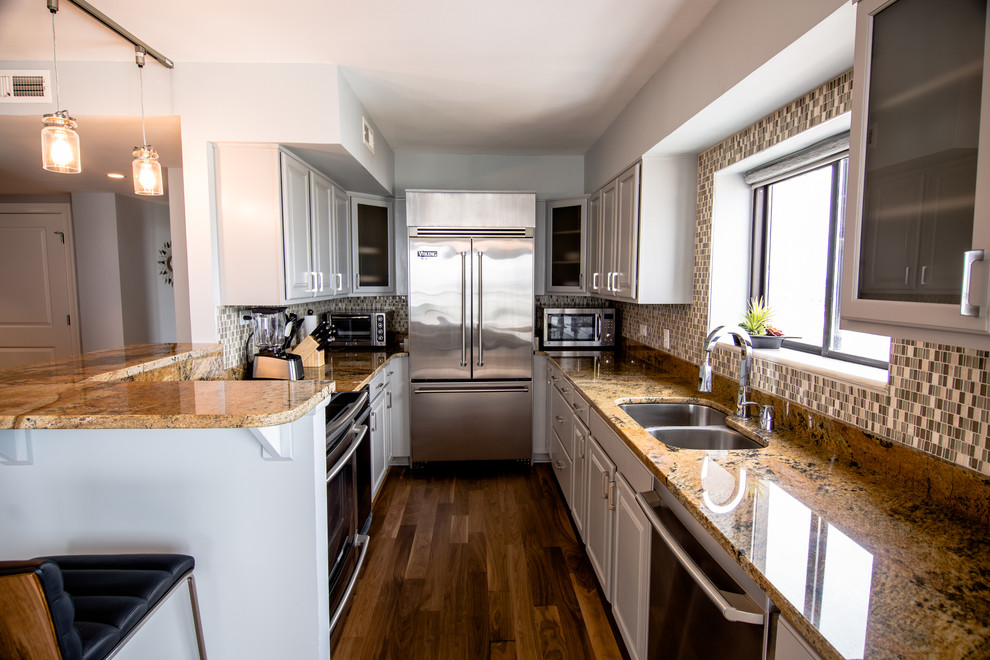 Small contemporary galley kitchen in Other with a double-bowl sink, glass-front cabinets, grey cabinets, granite worktops, multi-coloured splashback, glass sheet splashback, stainless steel appliances, medium hardwood flooring and a breakfast bar.