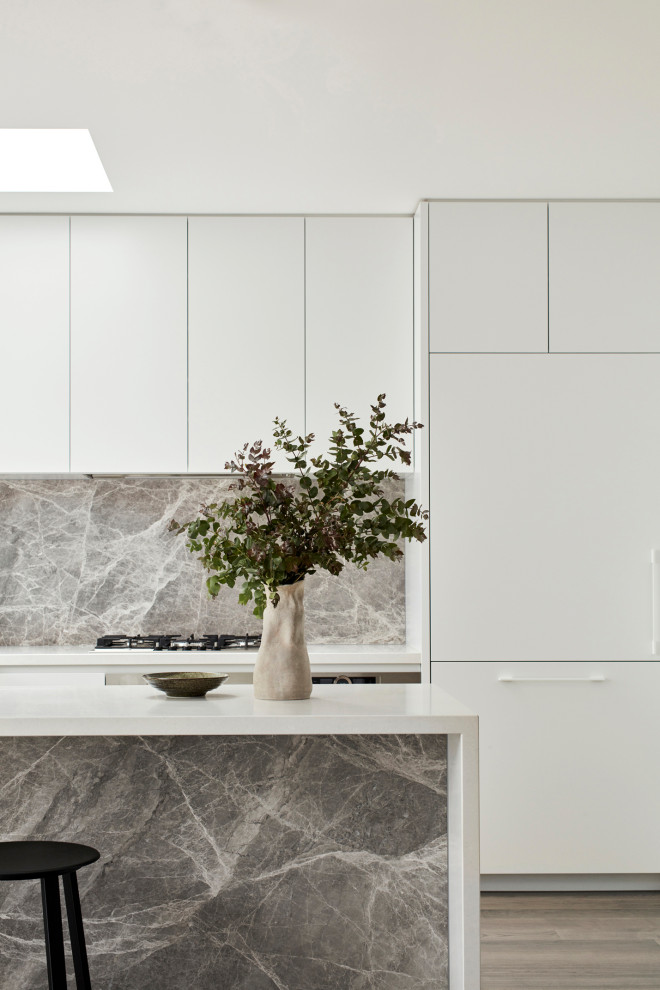Inspiration för ett mellanstort funkis vit vitt kök, med en undermonterad diskho, släta luckor, vita skåp, bänkskiva i kvarts, grått stänkskydd, stänkskydd i sten, rostfria vitvaror, mellanmörkt trägolv, en halv köksö och brunt golv
