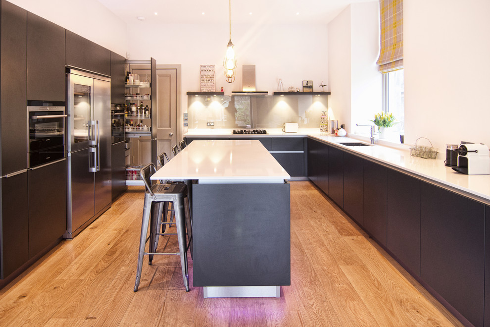 Moderne Küche in U-Form mit Unterbauwaschbecken, flächenbündigen Schrankfronten, schwarzen Schränken, Küchengeräten aus Edelstahl, braunem Holzboden und Kücheninsel in Edinburgh