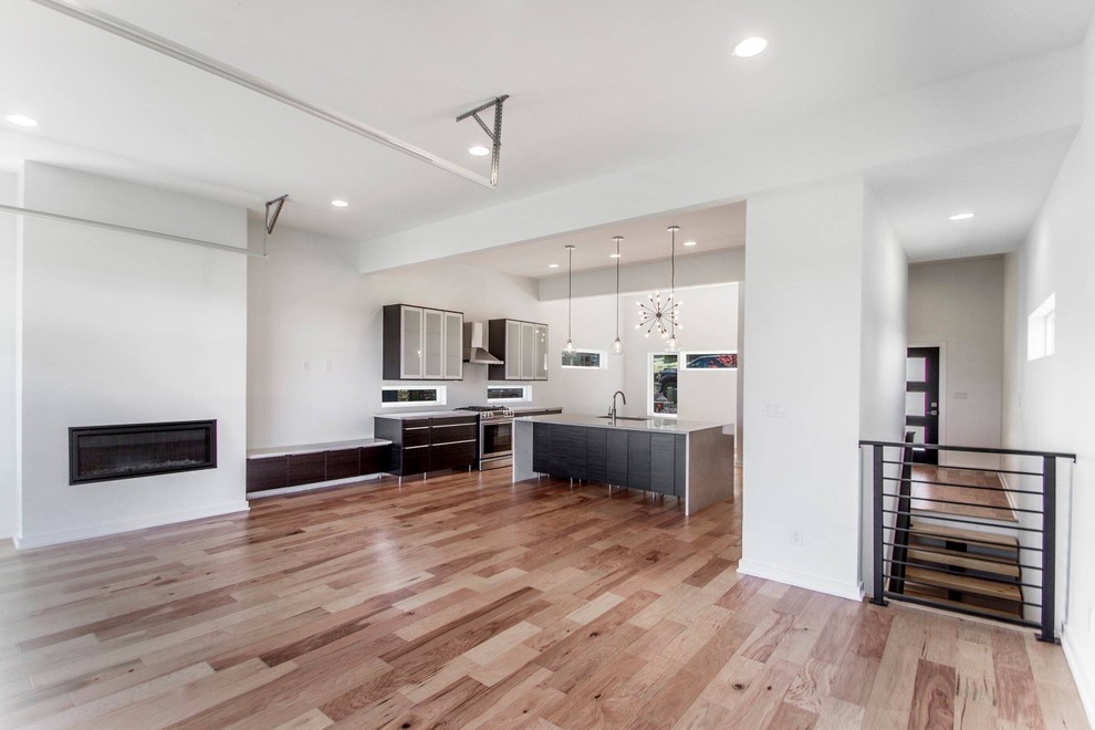 Bild på ett mellanstort funkis vit vitt kök och matrum, med en enkel diskho, släta luckor, skåp i mörkt trä, bänkskiva i kvarts, rostfria vitvaror, ljust trägolv, en köksö och brunt golv
