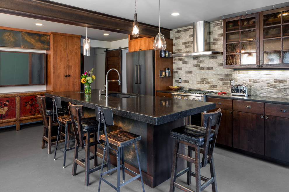 Bild på ett stort funkis linjärt kök och matrum, med en dubbel diskho, luckor med glaspanel, grått stänkskydd, svarta vitvaror, en köksö, skåp i mörkt trä, granitbänkskiva, stänkskydd i stenkakel och betonggolv