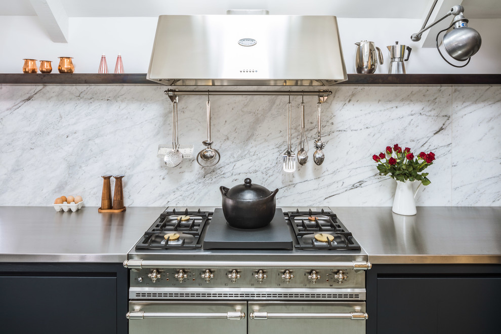 Example of a large trendy l-shaped gray floor open concept kitchen design in Other with an integrated sink, flat-panel cabinets, black cabinets, stainless steel countertops, white backsplash, marble backsplash, stainless steel appliances and an island
