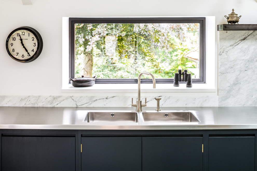 Foto på ett stort funkis kök, med en integrerad diskho, släta luckor, svarta skåp, bänkskiva i rostfritt stål, vitt stänkskydd, stänkskydd i marmor, rostfria vitvaror, en köksö och grått golv