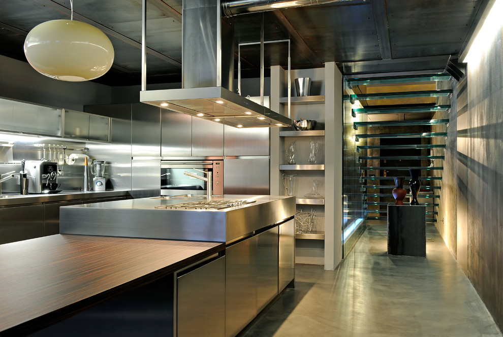 ミラノにある広いインダストリアルスタイルのおしゃれなキッチン (フラットパネル扉のキャビネット、ステンレスキャビネット、メタリックのキッチンパネル、メタルタイルのキッチンパネル、シルバーの調理設備、一体型シンク、ステンレスカウンター、コンクリートの床) の写真
