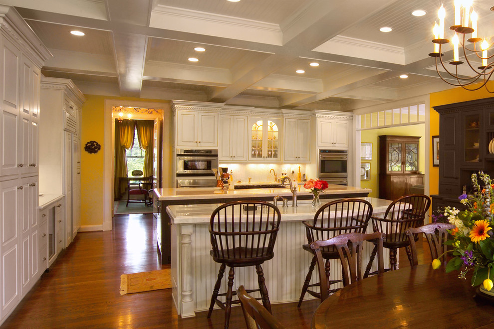 Klassische Küche mit weißen Schränken, Marmor-Arbeitsplatte, Küchenrückwand in Weiß, Küchengeräten aus Edelstahl, braunem Holzboden und zwei Kücheninseln in Louisville