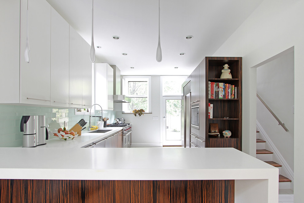 Cette photo montre une cuisine tendance en L et bois foncé avec un placard à porte plane, une crédence en carreau de verre et un électroménager en acier inoxydable.