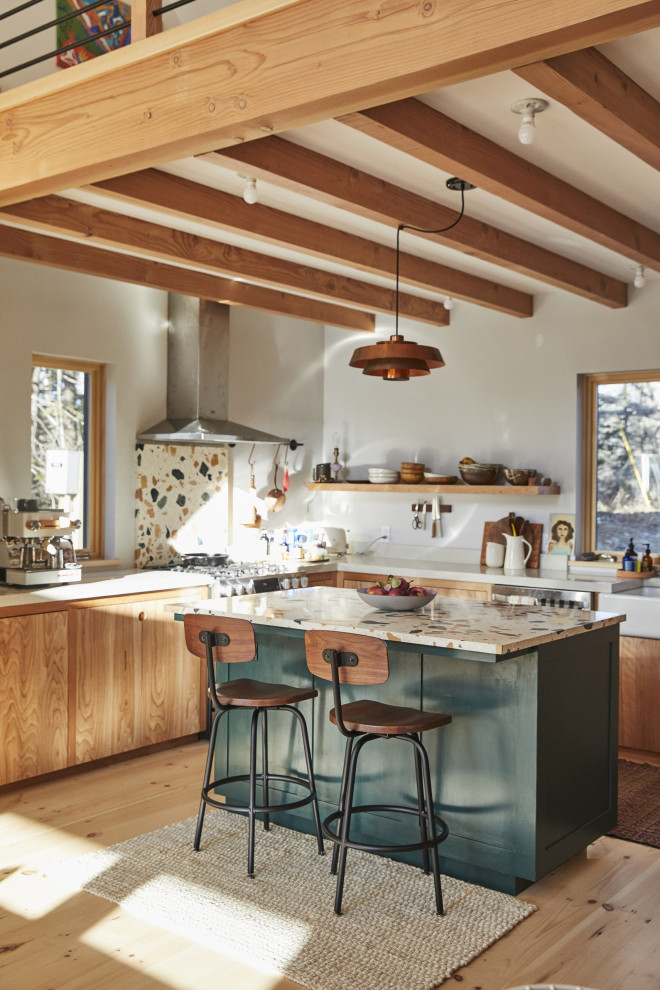 Cette photo montre une cuisine ouverte tendance en L et bois clair de taille moyenne avec un évier de ferme, un placard à porte plane, un plan de travail en terrazzo, une crédence blanche, un électroménager en acier inoxydable, parquet clair, îlot, un plan de travail blanc et poutres apparentes.