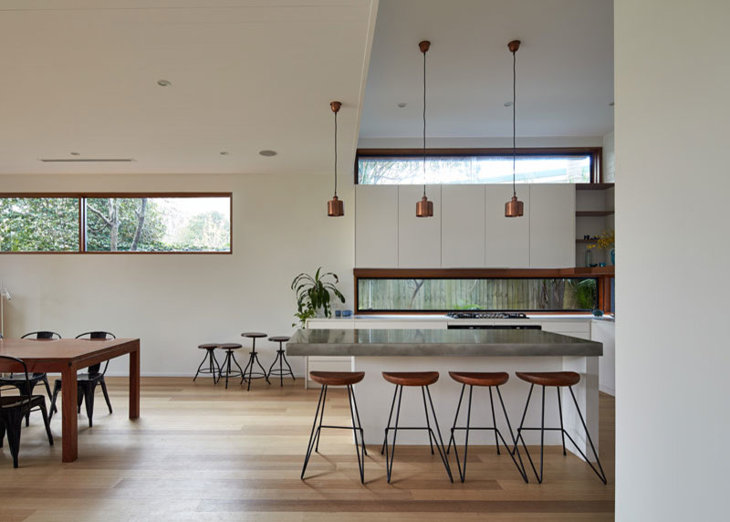 Photo of a medium sized contemporary l-shaped kitchen/diner in Sydney with a double-bowl sink, flat-panel cabinets, white cabinets, concrete worktops, black splashback, ceramic splashback, stainless steel appliances, light hardwood flooring and an island.