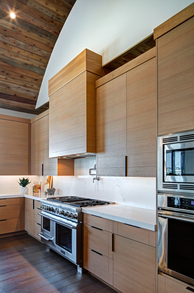Inspiration for a large contemporary u-shaped kitchen/diner in Salt Lake City with a belfast sink, flat-panel cabinets, light wood cabinets, engineered stone countertops, white splashback, stainless steel appliances, medium hardwood flooring, an island, brown floors and white worktops.