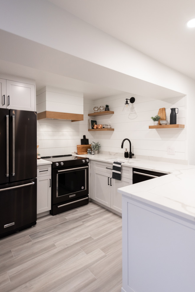 モントリオールにある高級な小さなカントリー風のおしゃれなキッチン (シングルシンク、シェーカースタイル扉のキャビネット、白いキャビネット、珪岩カウンター、白いキッチンパネル、木材のキッチンパネル、黒い調理設備、アイランドなし、グレーの床、白いキッチンカウンター、ラミネートの床) の写真