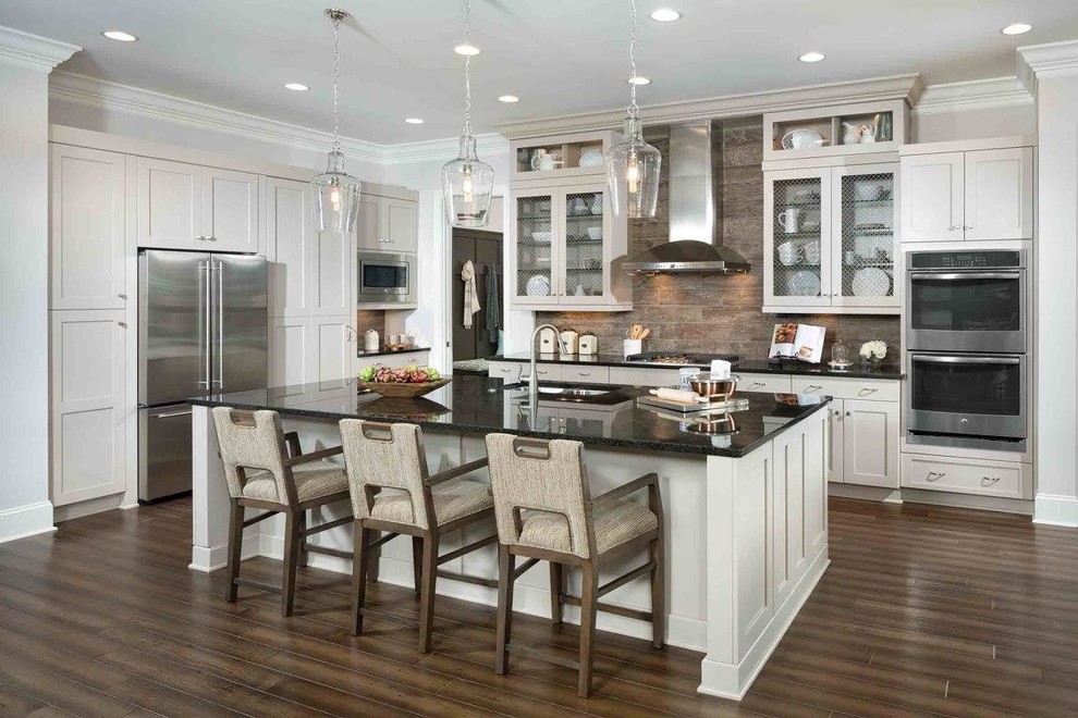 Photo of a beach style kitchen in Other with a submerged sink, shaker cabinets, beige cabinets, brown splashback, stainless steel appliances, an island and brown floors.