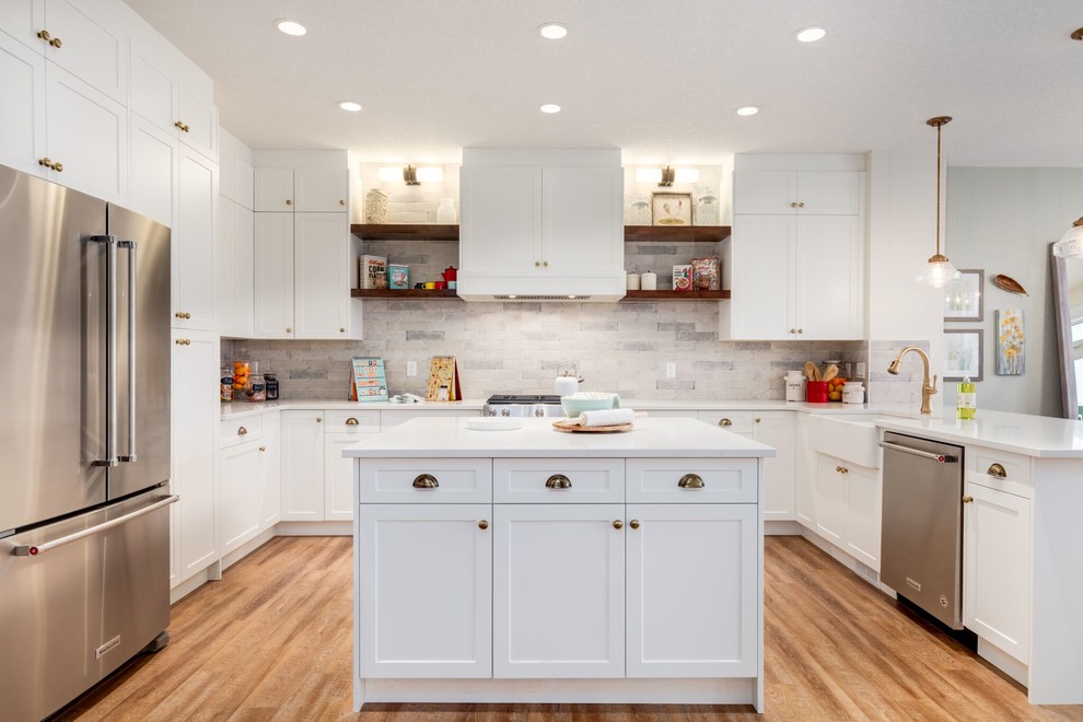Inspiration for a transitional u-shaped medium tone wood floor and brown floor eat-in kitchen remodel in Calgary with a farmhouse sink, shaker cabinets, white cabinets, gray backsplash, stone tile backsplash, stainless steel appliances and an island