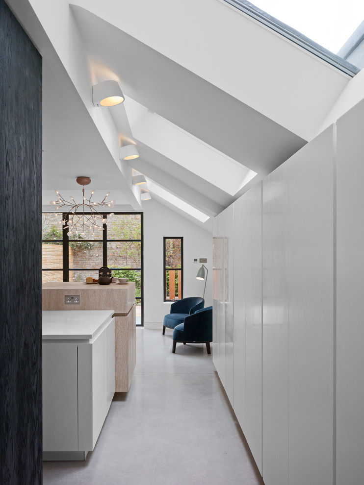 Inspiration for a mid-sized contemporary galley concrete floor and gray floor eat-in kitchen remodel in London with an integrated sink, flat-panel cabinets, white cabinets, solid surface countertops, white backsplash, paneled appliances and an island