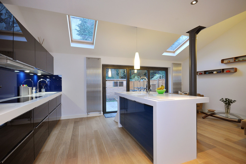 Пример оригинального дизайна: кухня-гостиная в современном стиле с плоскими фасадами, синим фартуком и фартуком из стекла