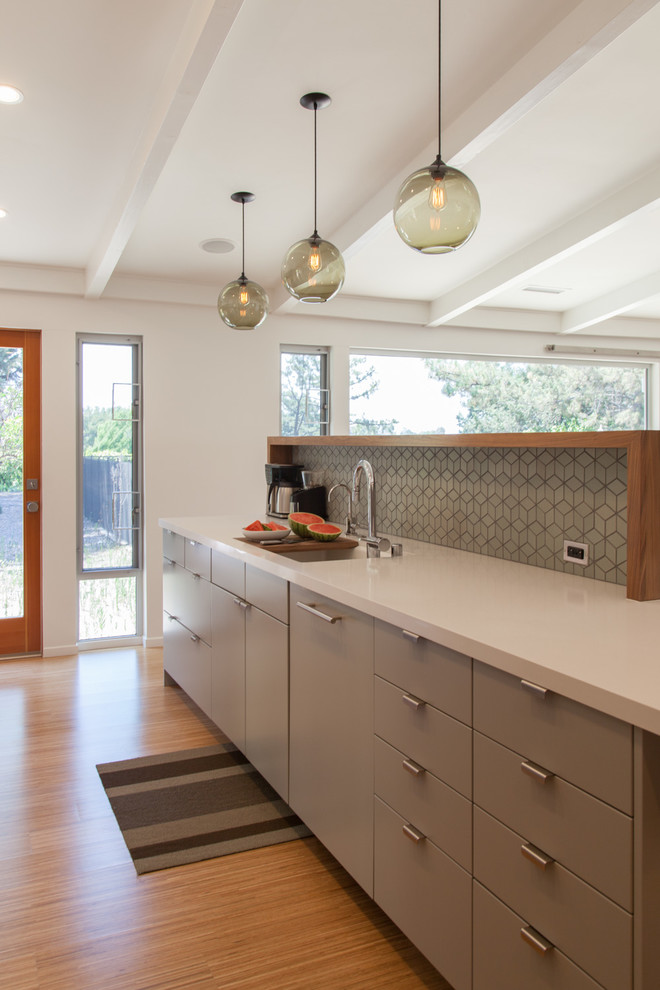 This is an example of a midcentury galley open plan kitchen in Los Angeles with a single-bowl sink, flat-panel cabinets, grey cabinets, engineered stone countertops, grey splashback, ceramic splashback, integrated appliances and medium hardwood flooring.