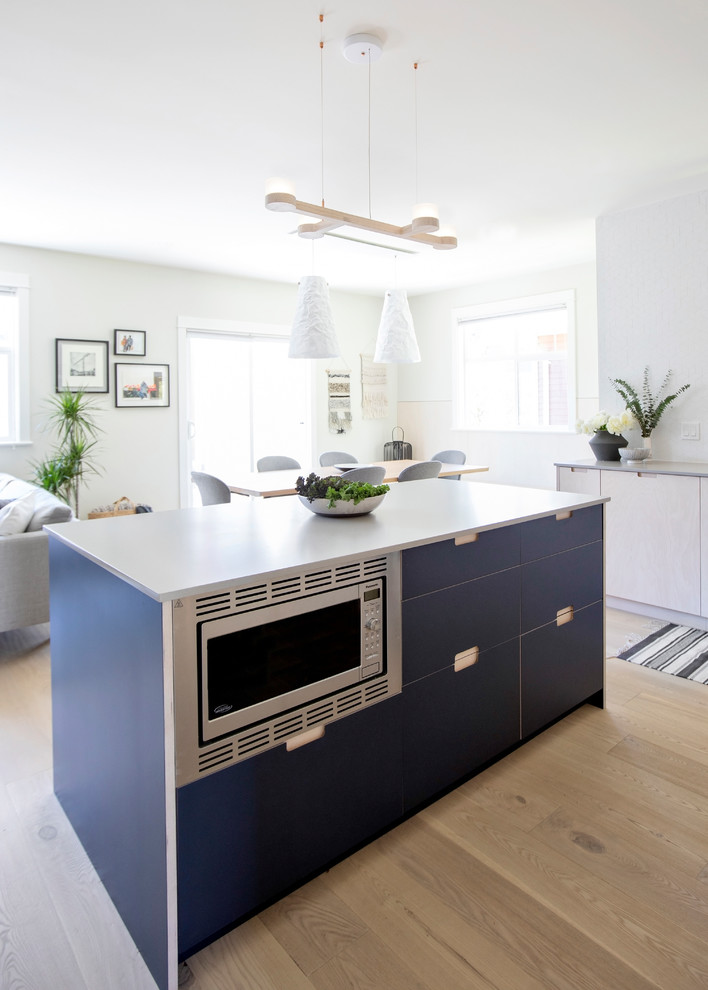 Foto på ett litet minimalistiskt grå kök, med en dubbel diskho, släta luckor, blå skåp, bänkskiva i kvarts, vitt stänkskydd, stänkskydd i porslinskakel, rostfria vitvaror, ljust trägolv och en köksö