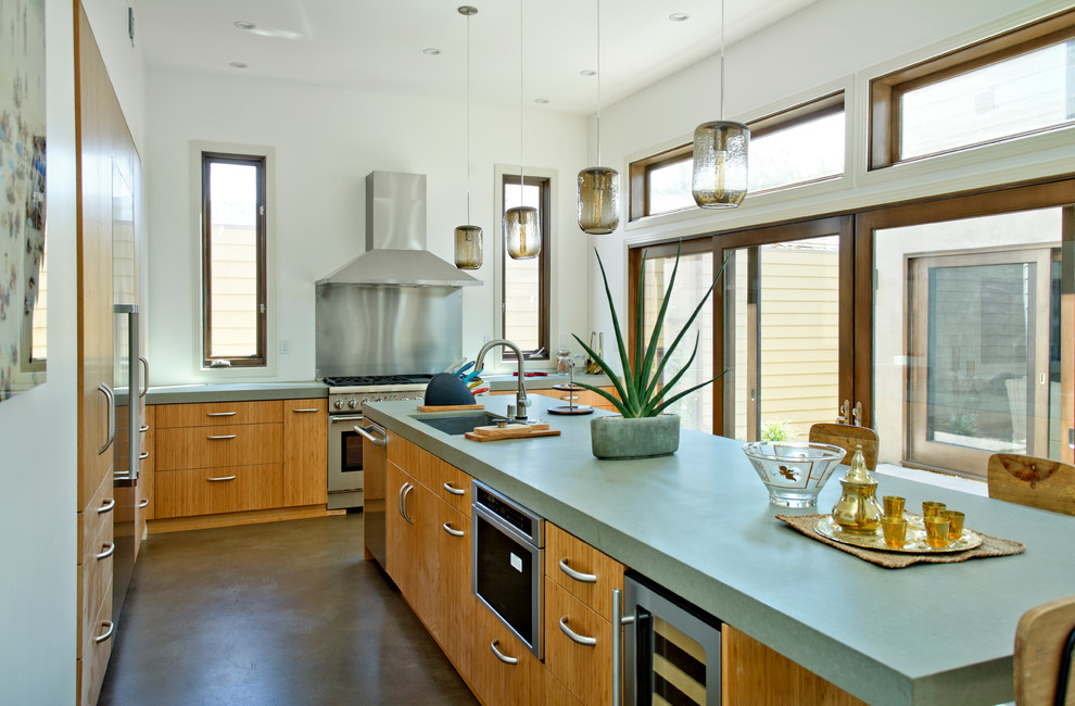 Bild på ett funkis kök, med släta luckor, skåp i mellenmörkt trä, bänkskiva i betong, stänkskydd med metallisk yta, stänkskydd i metallkakel och rostfria vitvaror