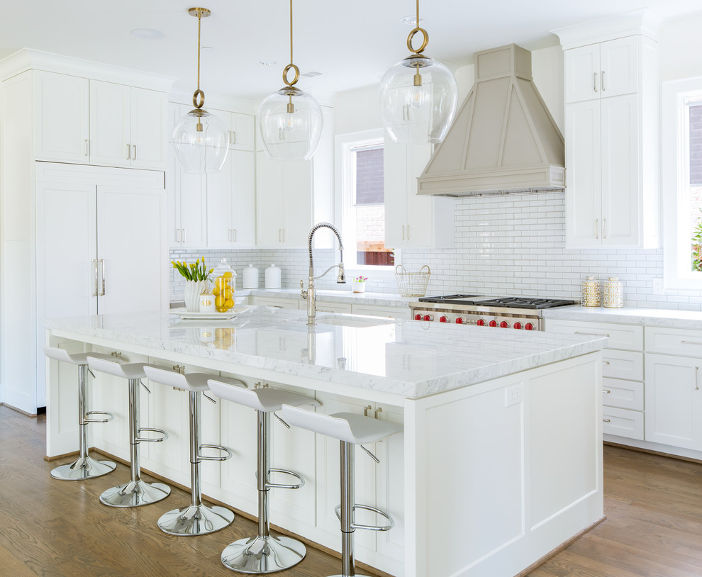 Klassisk inredning av ett stort vit vitt u-kök, med en undermonterad diskho, skåp i shakerstil, vita skåp, marmorbänkskiva, vitt stänkskydd, stänkskydd i tunnelbanekakel, integrerade vitvaror, en köksö, mellanmörkt trägolv och brunt golv