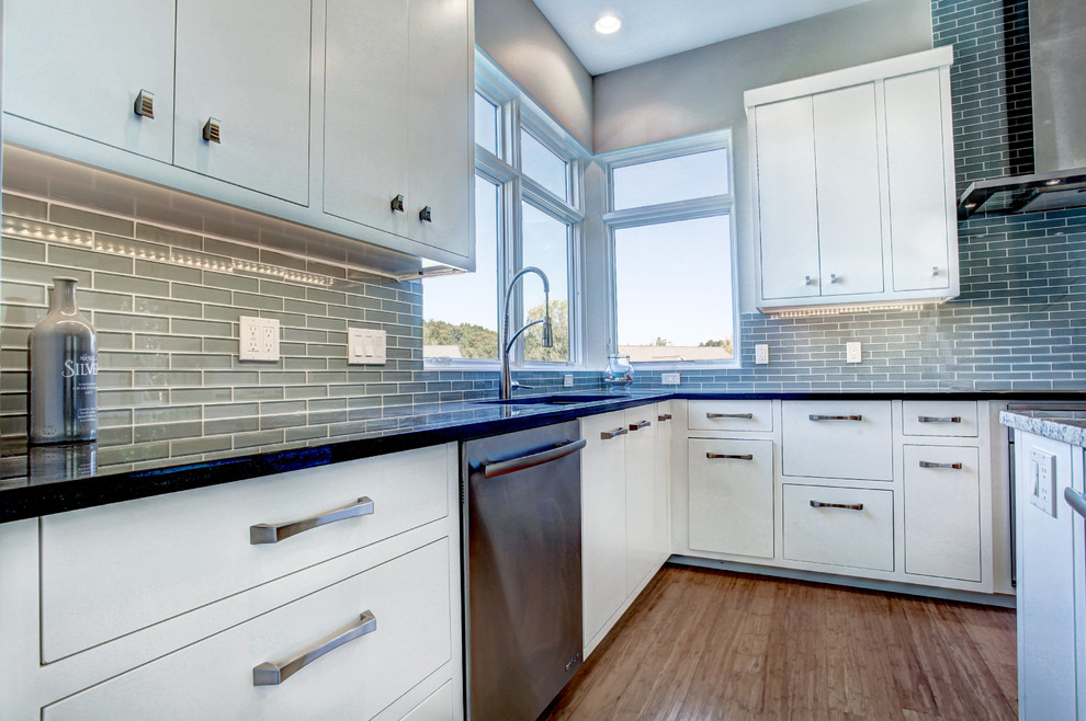 Exempel på ett stort modernt kök, med en undermonterad diskho, släta luckor, vita skåp, blått stänkskydd, stänkskydd i glaskakel, rostfria vitvaror, bambugolv, en köksö och bänkskiva i kvarts