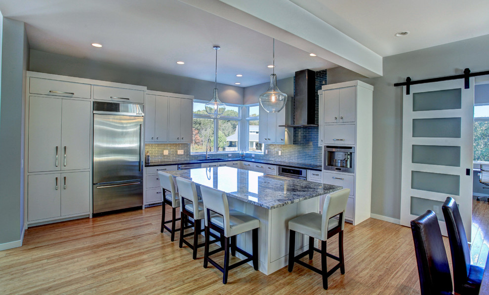Trendy l-shaped eat-in kitchen photo in Grand Rapids with an undermount sink, flat-panel cabinets, white cabinets, granite countertops, glass tile backsplash and stainless steel appliances