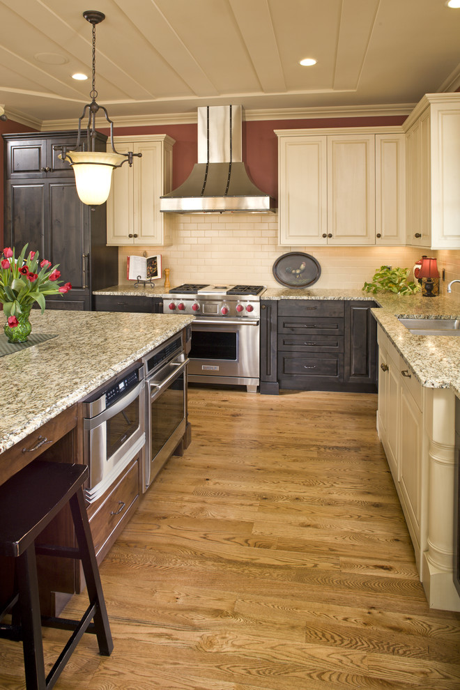 Photo of a large rural l-shaped kitchen/diner in Minneapolis with a submerged sink, raised-panel cabinets, beige cabinets, granite worktops, beige splashback, stainless steel appliances, medium hardwood flooring and an island.