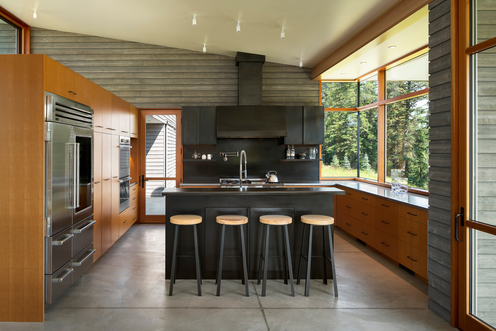 Foto på ett mellanstort funkis grå kök, med släta luckor, skåp i mellenmörkt trä, bänkskiva i rostfritt stål, svart stänkskydd, stänkskydd i metallkakel, rostfria vitvaror, betonggolv, en köksö och grått golv