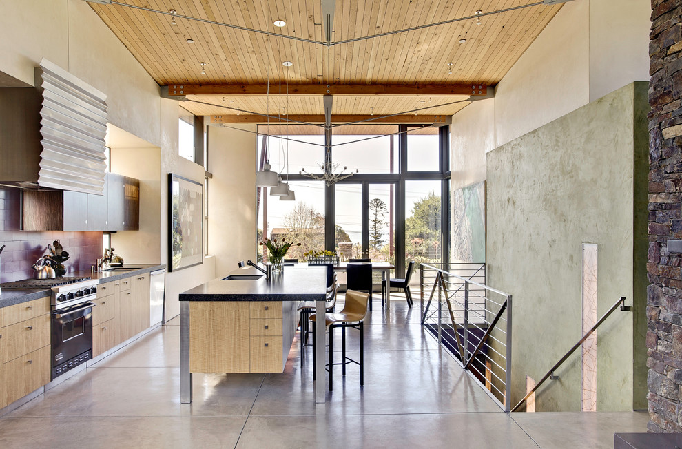 Example of a beach style galley concrete floor eat-in kitchen design in San Francisco with flat-panel cabinets, light wood cabinets, granite countertops, subway tile backsplash, black appliances, an undermount sink and an island