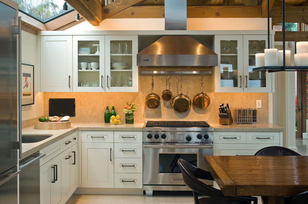 Foto de cocina costera con armarios tipo vitrina, electrodomésticos de acero inoxidable y salpicadero de piedra caliza