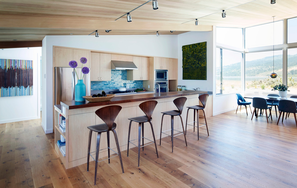 Photo of a contemporary galley kitchen in San Francisco with flat-panel cabinets, light wood cabinets, blue splashback, stainless steel appliances, medium hardwood flooring and an island.