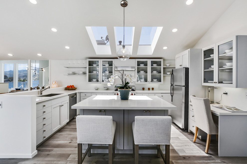 Beach style u-shaped brown floor open concept kitchen photo in San Francisco with an undermount sink, glass-front cabinets, gray cabinets, white backsplash, stainless steel appliances, an island and white countertops