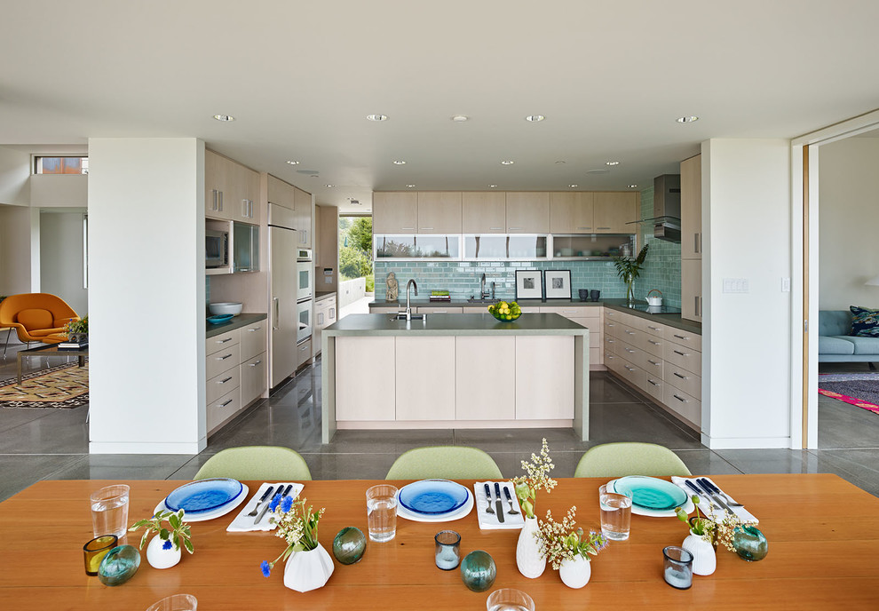 Cette image montre une cuisine américaine encastrable minimaliste en U et bois clair avec un évier encastré, un placard à porte plane, une crédence bleue et une crédence en carreau de verre.