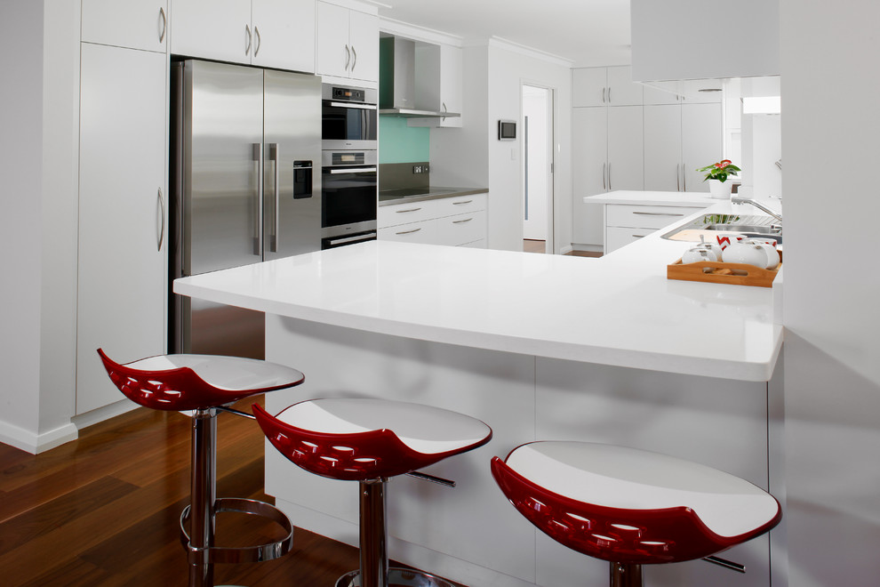 Idéer för ett modernt vit kök, med släta luckor, vita skåp, bänkskiva i kvarts, blått stänkskydd, glaspanel som stänkskydd och rostfria vitvaror