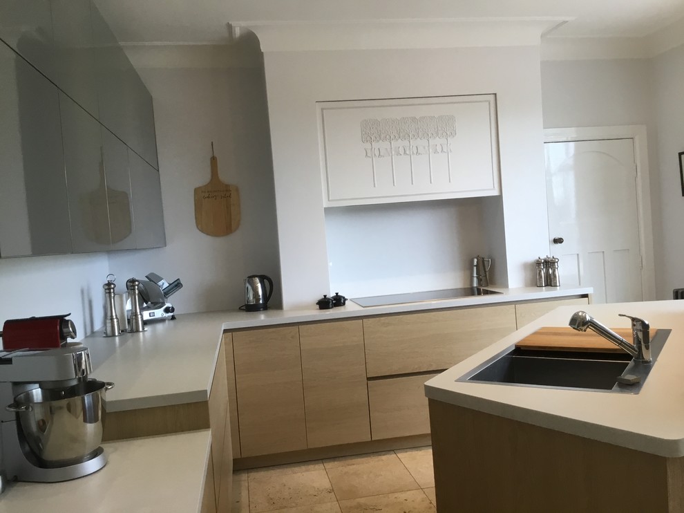 Photo of a medium sized contemporary l-shaped kitchen/diner in Manchester with a built-in sink, flat-panel cabinets, grey cabinets, laminate countertops, black appliances, limestone flooring, an island and beige floors.