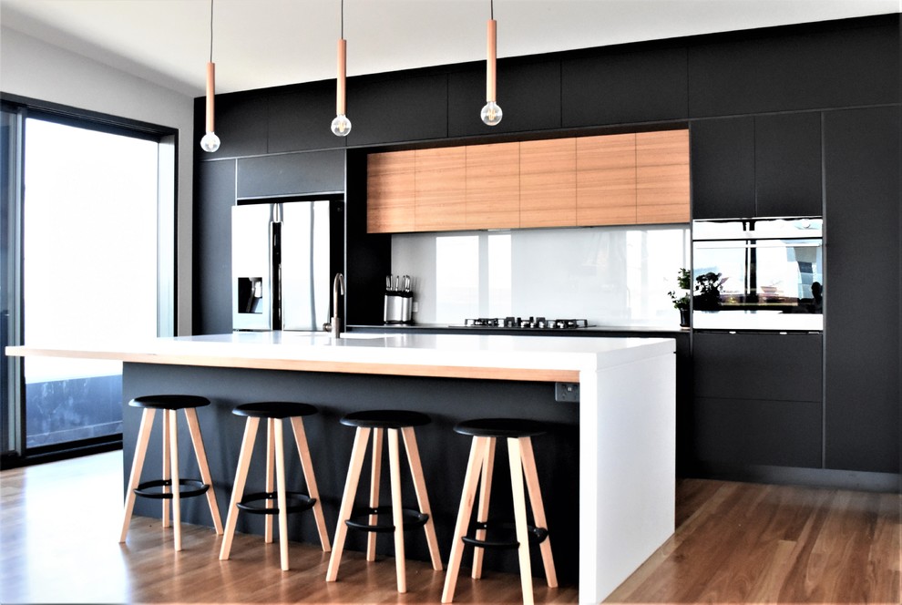 Bild på ett mellanstort funkis grå grått kök, med en undermonterad diskho, släta luckor, svarta skåp, bänkskiva i betong, vitt stänkskydd, glaspanel som stänkskydd, rostfria vitvaror, mellanmörkt trägolv, en köksö och brunt golv