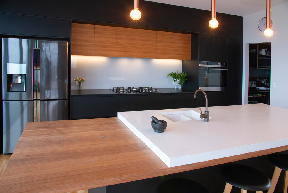 Idéer för att renovera ett mellanstort funkis grå grått kök, med en undermonterad diskho, släta luckor, svarta skåp, bänkskiva i betong, vitt stänkskydd, glaspanel som stänkskydd, rostfria vitvaror, mellanmörkt trägolv, en köksö och brunt golv