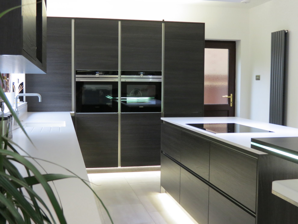 Photo of a medium sized contemporary l-shaped open plan kitchen in Sussex with an integrated sink, flat-panel cabinets, dark wood cabinets, composite countertops, white splashback, stainless steel appliances and an island.