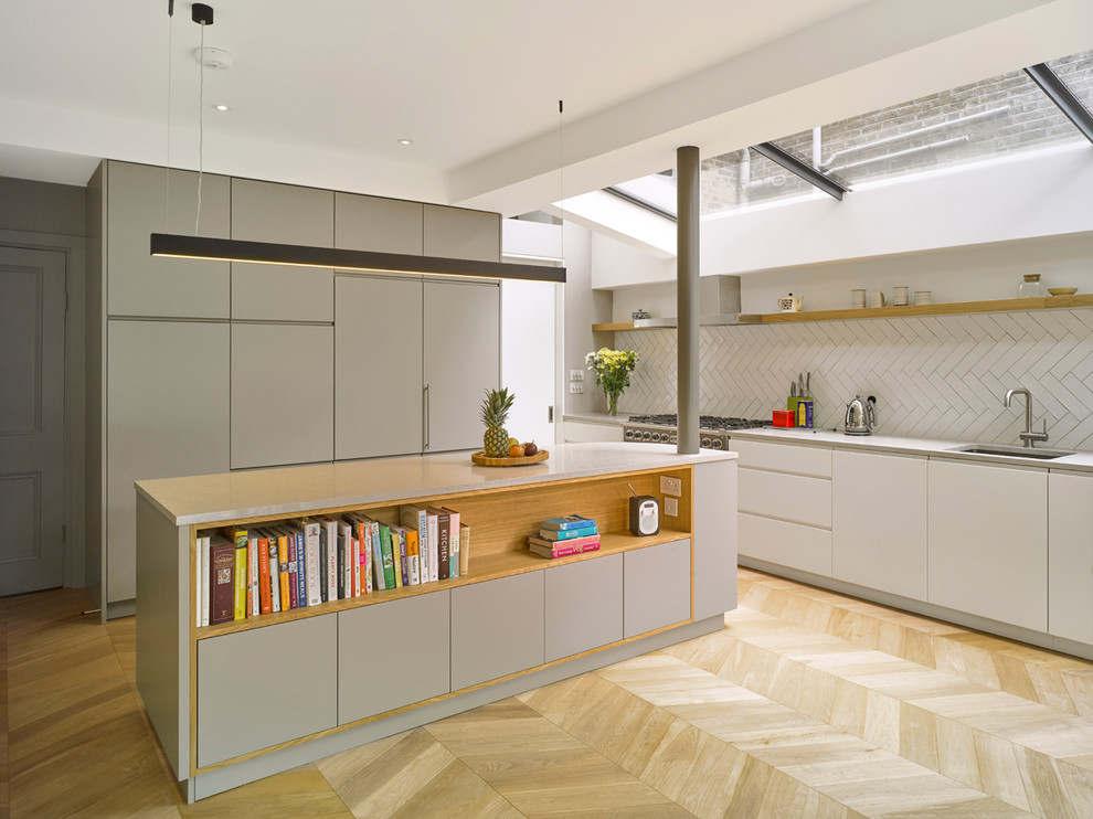 Medium sized contemporary single-wall kitchen/diner in London with a submerged sink, flat-panel cabinets, white cabinets, white splashback, metro tiled splashback, integrated appliances, light hardwood flooring, an island and beige floors.